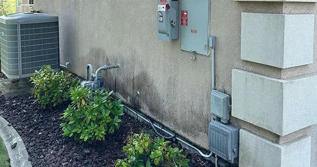 Air conditioning unit and electrical panel on exterior wall with landscaped shrubs.