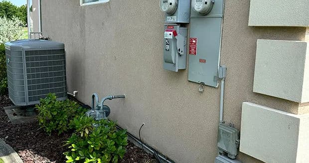 Electric meters and HVAC unit on the exterior wall of a residential building.